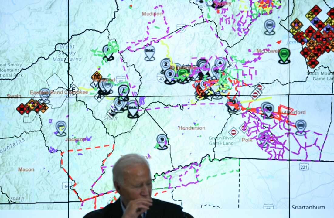 President Biden talks to state officials at an emergency operations center in Raleigh, NC, with a map of the area hit by Hurricane Helene behind him.