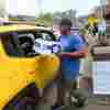 In this photo, Tony J. Daniel holds a case of bottled water and hands out the bottle through the open back window of a yellow SUV in Old Fort, NC, after Hurricane Helene on Sunday.